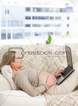 Relaxed pregnant woman using her laptop on the sofa 