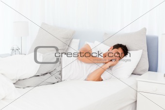 Sick man blowing his nose lying on his bed 
