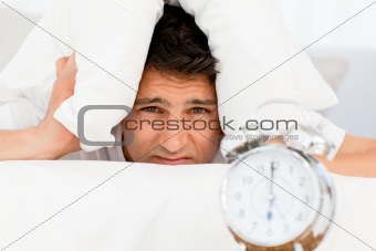 Sad man with head under the pillow waiting for his alarm clock