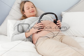 Happy future mom putting headphones on her belly
