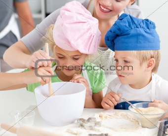 Two children and their mother stiring a preparation for cookies 