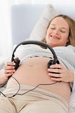 Happy pregnant woman putting headphones on her belly