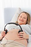 Adorable pregnant woman putting headphones on her belly