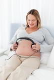 Adorable future mom putting headphones on her belly