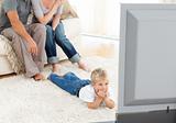 Attentive little boy watching television lying on the floor