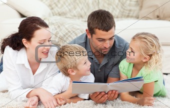 Family reading a book together lying on the floor at home