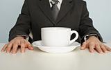 Huge cup of coffee on table near businessman