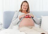 Cheerful pregnant woman putting baby shoes on her belly