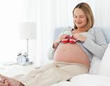 Cute pregnant woman putting baby shoes on her belly