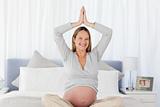 Smiling pregnant woman doing yoga on the bed 
