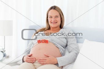 Pregnant woman resting on a bed with mom letters