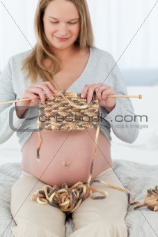 Pretty future mom knitting sitting in her bedroom at day