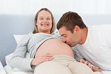 Happy man kissing the belly of his pregnant wife in the bed