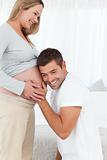 Happy man in knee listening to the belly of his pregnant wife