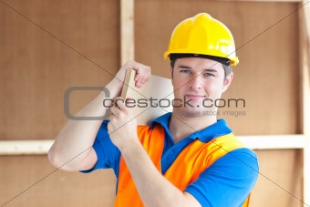 Confident young male worker with a yellow helmet carrying a wood