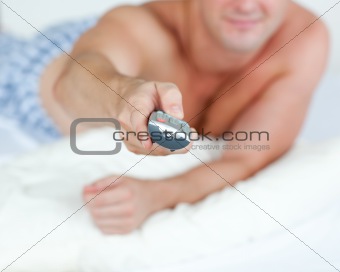 Close-up of a young man holding a remote lying on his bed