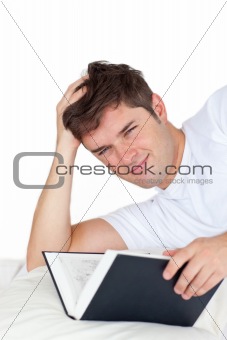 Smiling man reading a book lying on his bed
