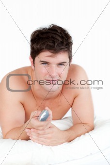 Handsome man lying on his bed and holding a remote