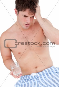 Dejected young man sitting on his bed and holding a glass of wat