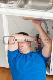 Tired man repairing his sink in the kitchen