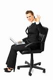Smiling modern business woman sitting on  chair with  laptop and showing ok gesture
