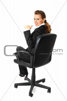 Smiling modern business woman sitting on chair and showing thumbs up gesture
