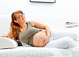 Smiling beautiful pregnant woman lying on  sofa and holding her belly
