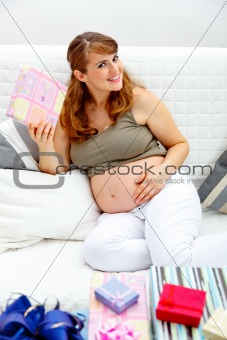 Smiling  beautiful pregnant woman sitting on sofa with gifts for her unborn baby
