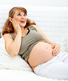 Happy beautiful pregnant woman sitting on sofa and holding her belly
