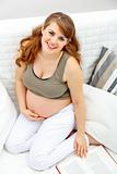 Smiling beautiful pregnant woman sitting on sofa with book

