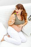 Smiling beautiful pregnant woman sitting on sofa and  eating pickle
