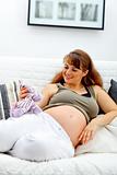 Smiling beautiful pregnant woman sitting on sofa and holding toy 

