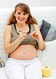 Smiling beautiful pregnant  female knitting for her baby
