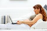 Pleased beautiful pregnant woman sitting on sofa with  laptop and credit card
