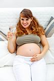 Smiling pregnant woman relaxing on sofa with  glass of water  in hand 
