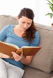 Attentive woman reading a book sitting on her sofa