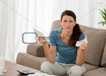 Serious woman holding bills while doing her accounts in the livi