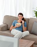 Happy woman eating pop corn while watching television on the sofa