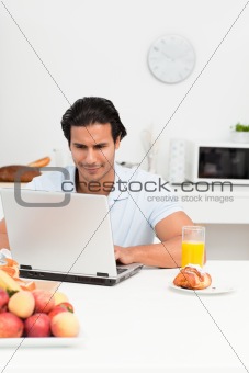 Charismatic hispanic man working on his laptop in the kitchen