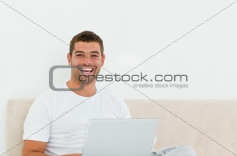 Happy man working on his laptop in his bedroom