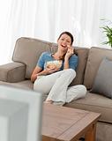 Cheerful woman watching television and eating pop corn