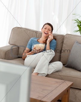 Cheerful woman watching television and eating pop corn