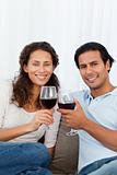 Happy couple clinking glasses of red wine on the sofa