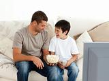 Father and son watching television while eating pop corn 