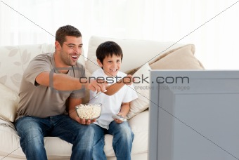 Happy father and son watching television while eating pop corn 