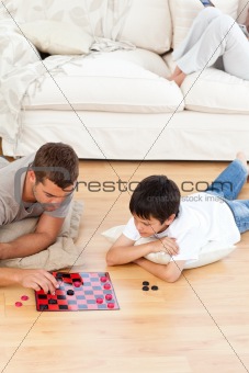 Father and son playing checkers together lying on the floor
