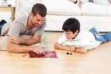Handsome man playing checkers with his son lying on the floor