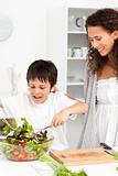 Cute boy mixing a salad with his mother in the kitchen