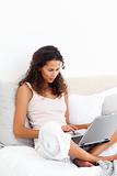 Attractive woman working on her laptop sitting on her bed 