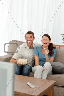 Cute couple eating pop corn while watching television on the sofa